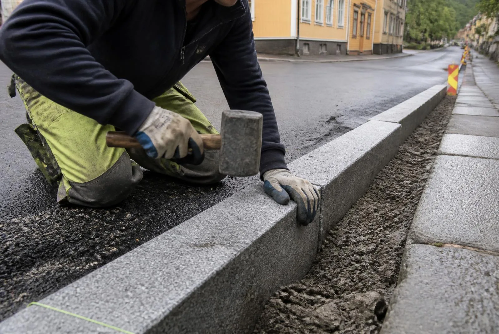 Arbetare som justerar granitkantsten längs en asfaltkant med klubba
